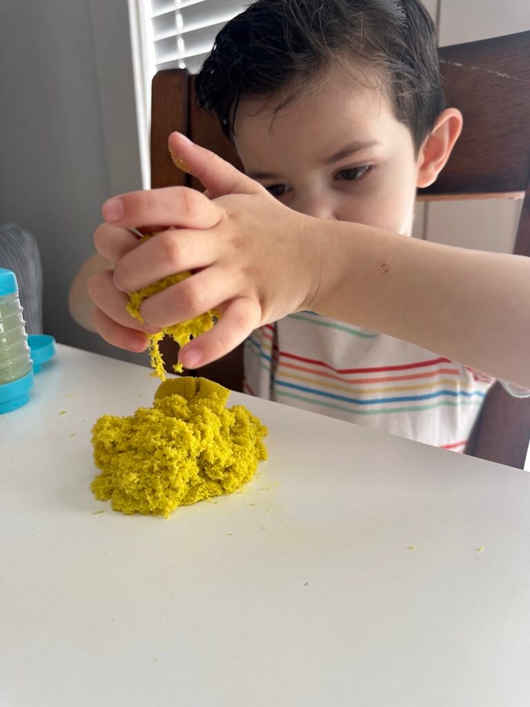 Young child squeezing and shaping bright yellow Wonder Factory Never Dry Dough on a table, enjoying hands-on sensory play with soft, moldable gluten-free dough.