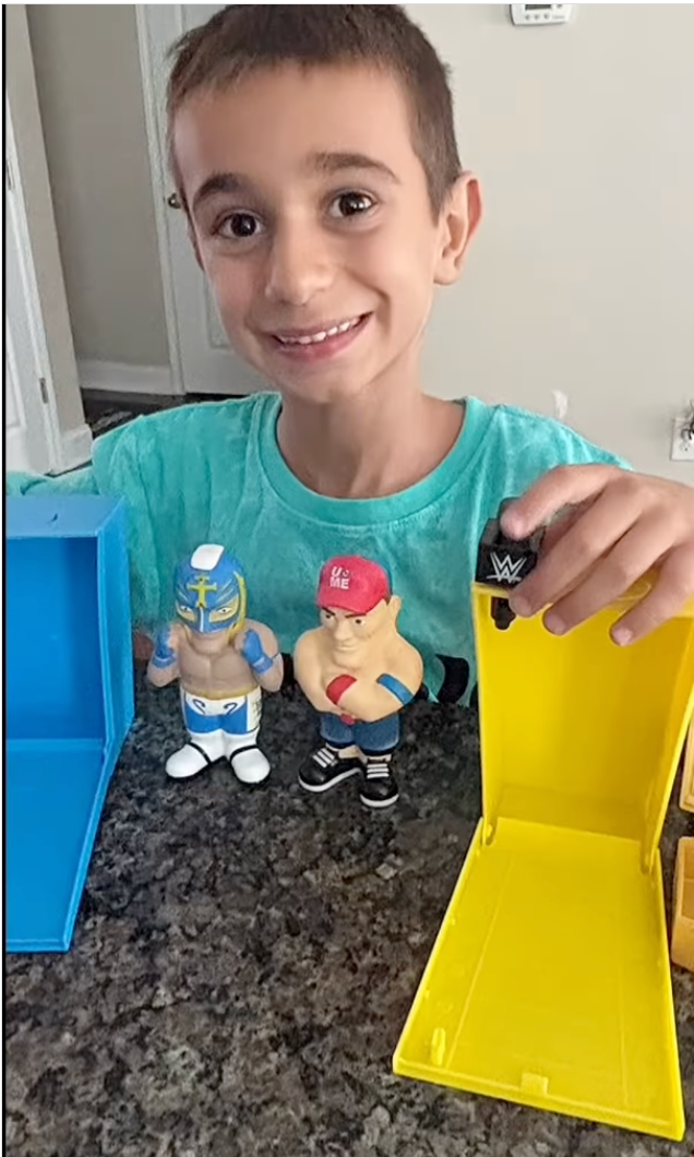 Child smiling while holding WWE Smash N Squish collectible figures next to colorful packaging cases on a kitchen counter